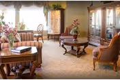 Cozy senior living facility lounge with plush seating, a coffee table, flowers, and a display cabinet.