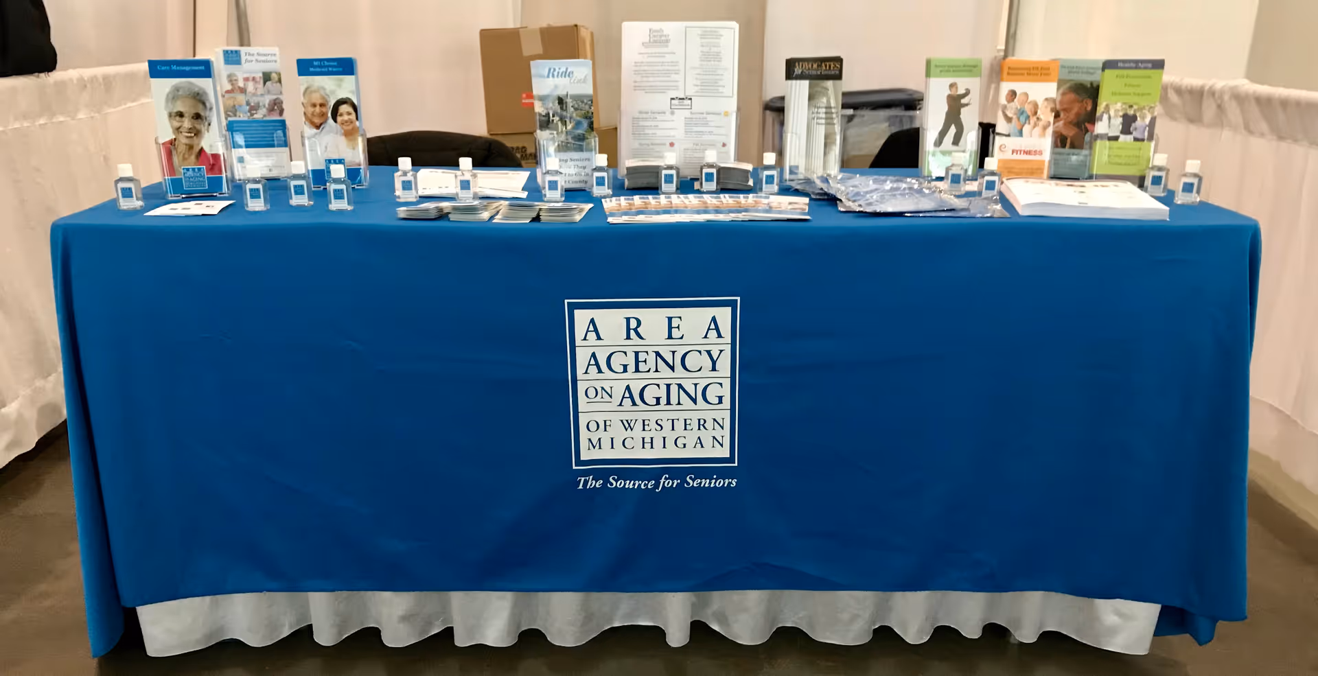 A blue cloth table displays brochures and signage for Area Agency on Aging of Western Michigan.