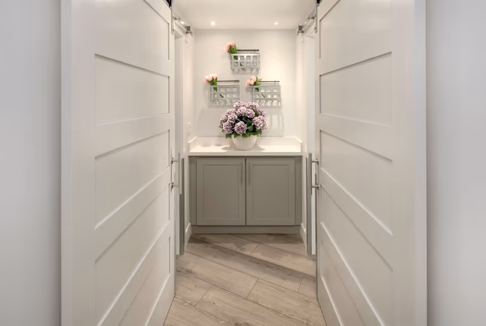 Bright hallway leading to a compact vanity area with flowers and storage cabinets.