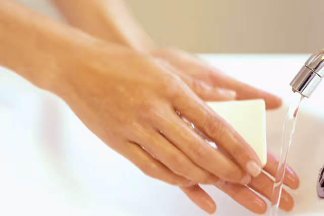 Hands washing under running water with soap at a bathroom sink.
