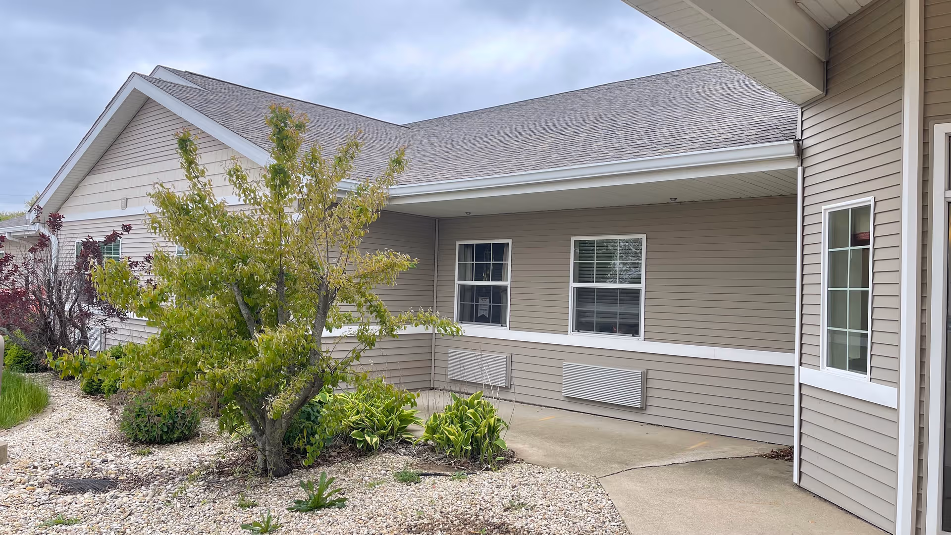 Exterior view of WoodRidge Supportive Living Geneseo building with beige siding and landscaped rocks.
