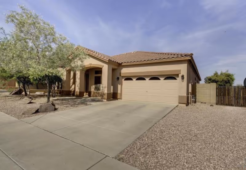 Single-story beige senior living home with tiled roof, attached garage, and desert landscaping.