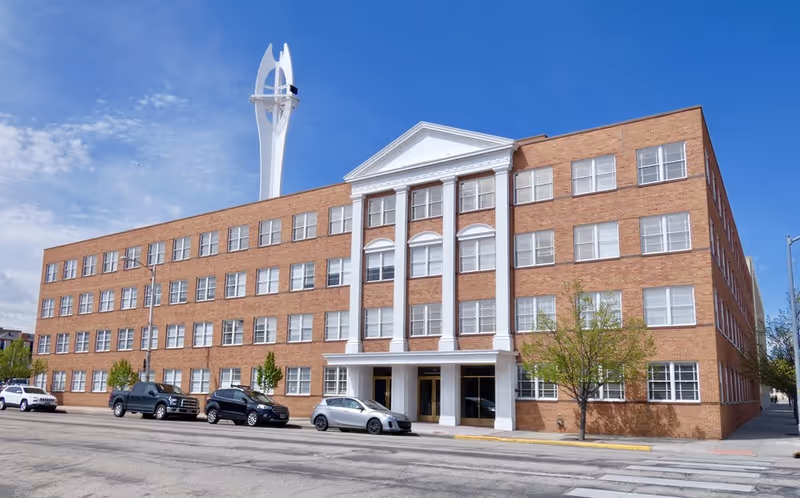 Brick, four-story senior living facility exterior with a central entrance and parked cars.