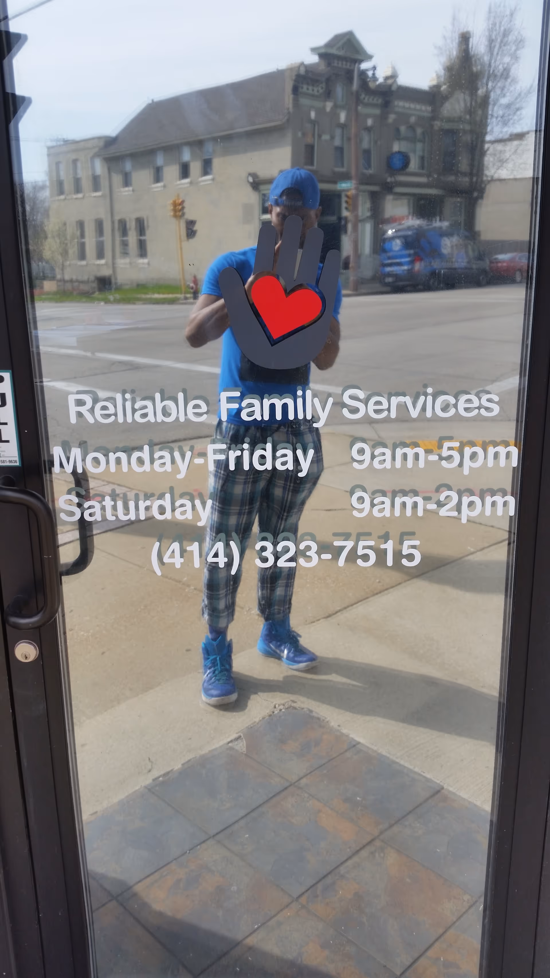 Reflection of a person in blue outside, glass door shows Reliable Family Services hours text.
