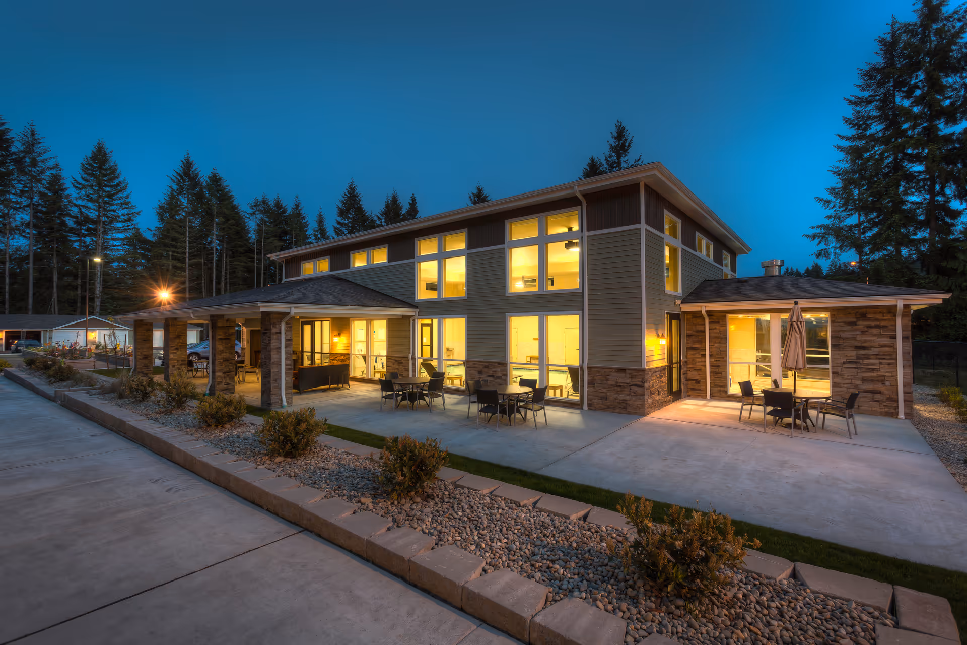 A modern senior living facility exterior at dusk with illuminated windows and outdoor seating.