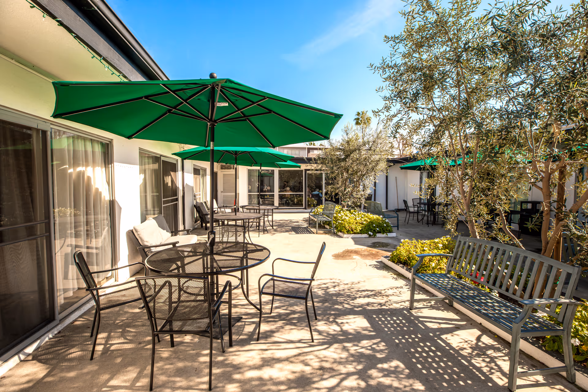 Outdoor courtyard at The Earlwood with green umbrellas, tables, chairs, and benches.