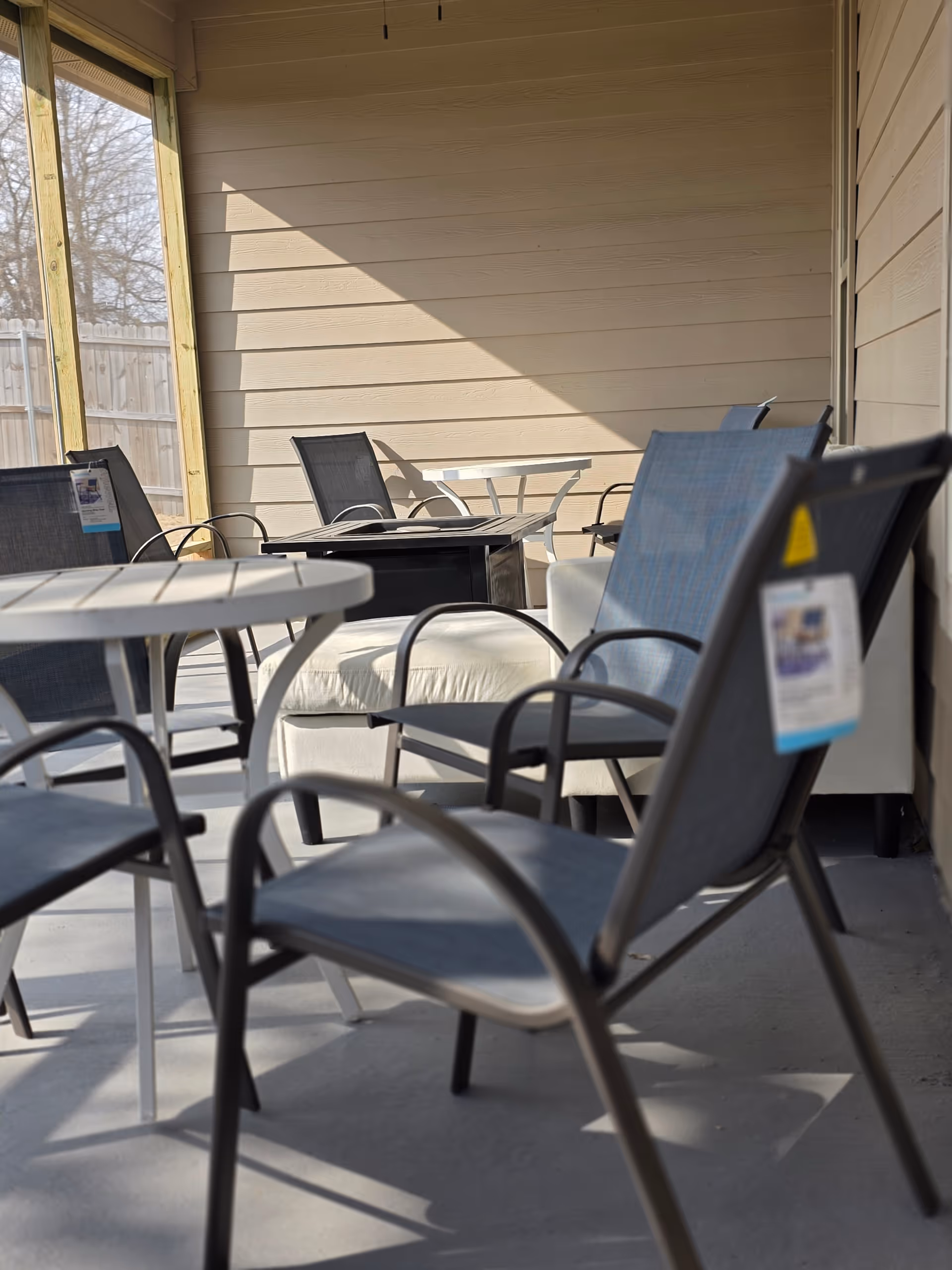 A covered outdoor patio with metal chairs, round tables, and a beige wall.