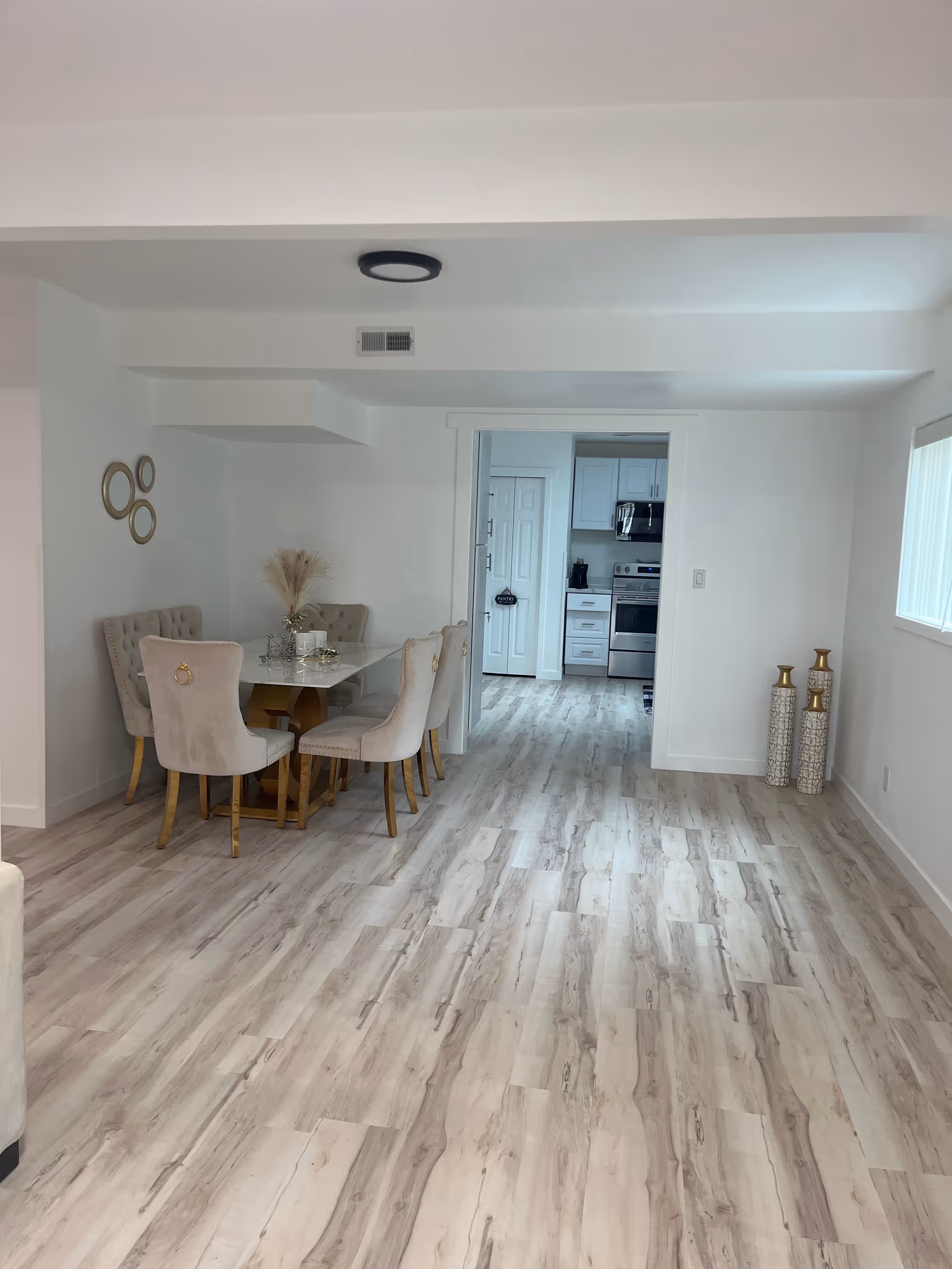 Bright dining area with glass table, beige chairs, and open kitchen doorway.