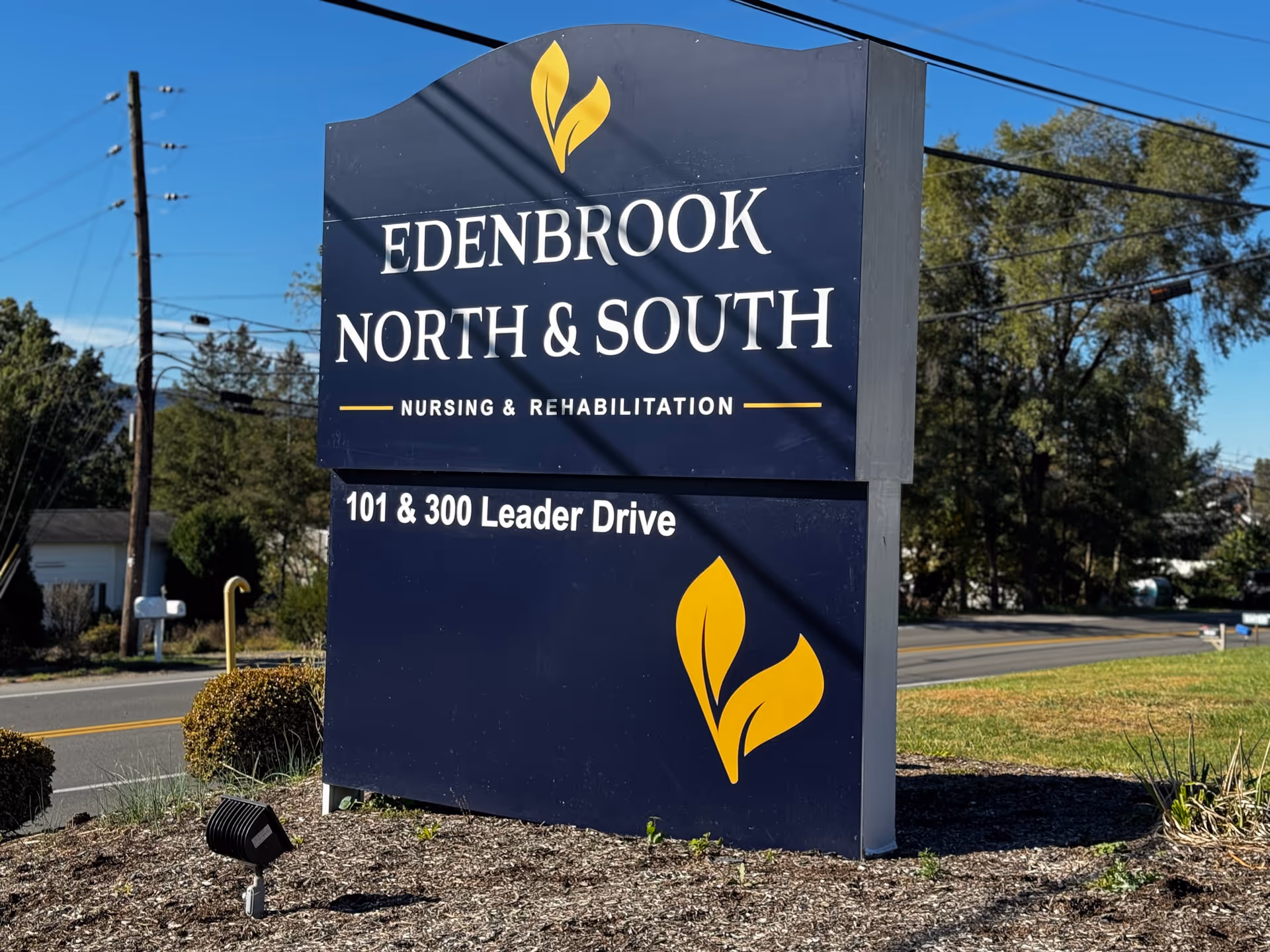Tall blue roadside sign for Edenbrook North & South Nursing & Rehabilitation with yellow leaves.