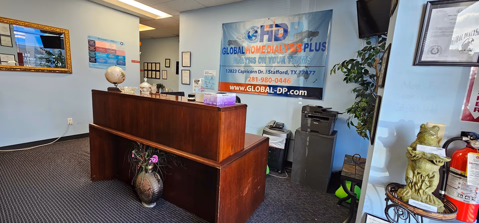 Reception area inside Global Home Dialysis Plus with wooden desk, banner, globe, and plants.
