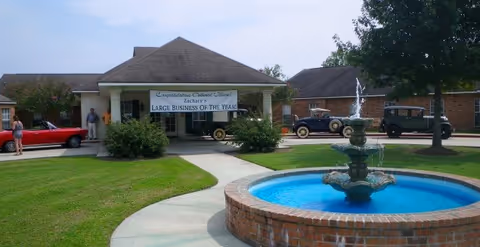 Exterior view of Oakwood Village facility with fountain, entrance, and parked cars.