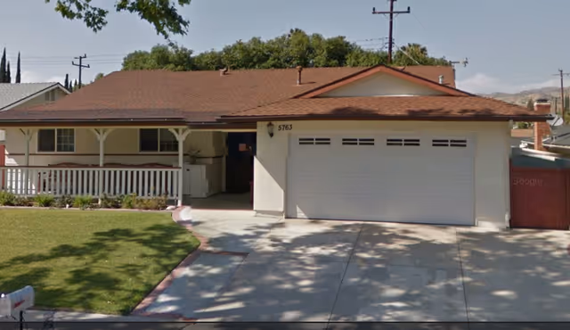 A single-story beige house with a two-car garage and front porch, lawn and driveway.