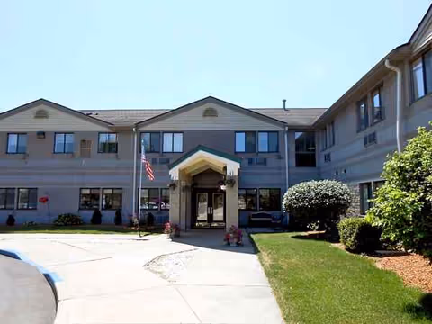 Wood Ridge Assisted Living exterior with entrance canopy, flag, and manicured landscaping.