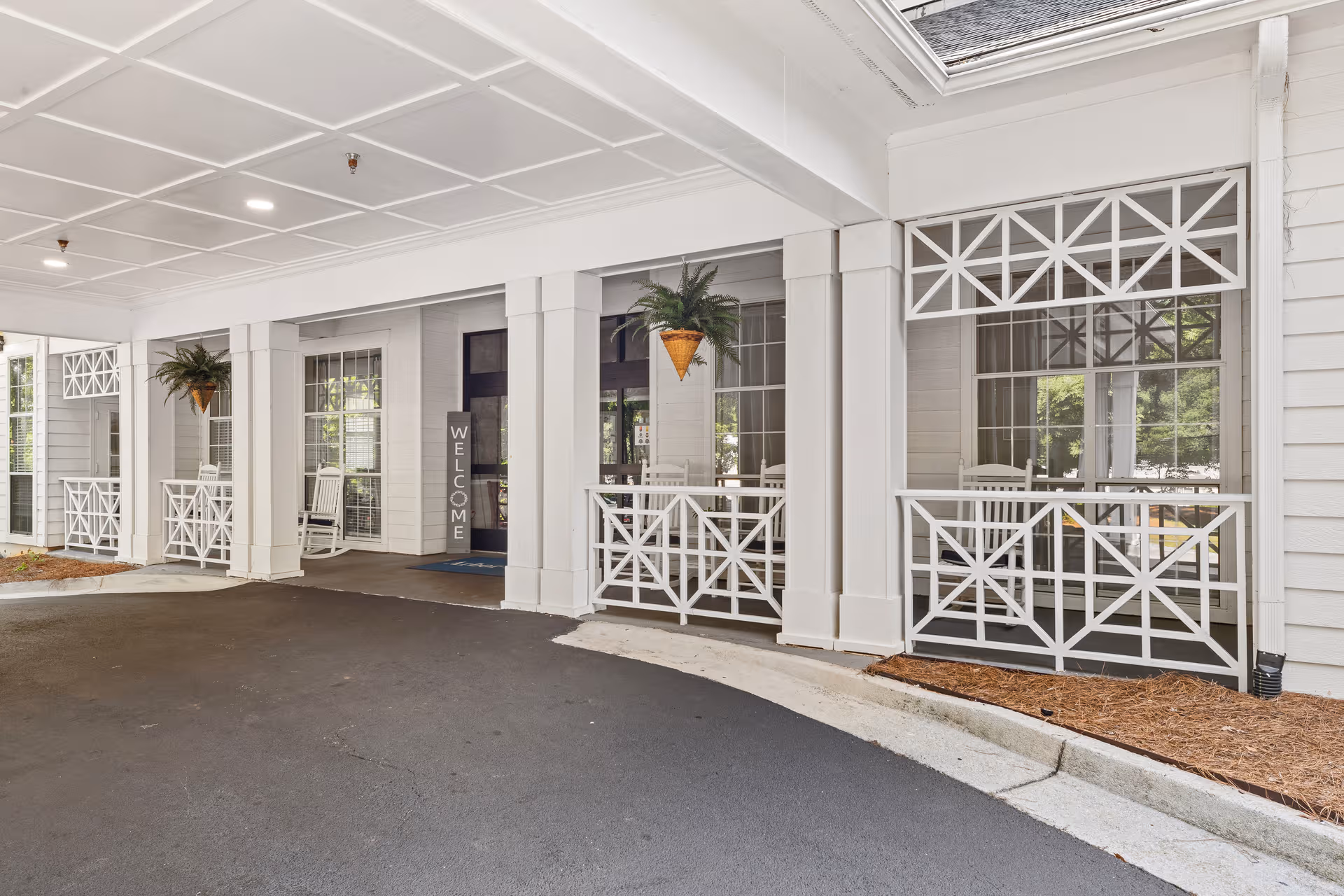 White covered entrance with columns, railings, and hanging ferns at Arbor Terrace Decatur