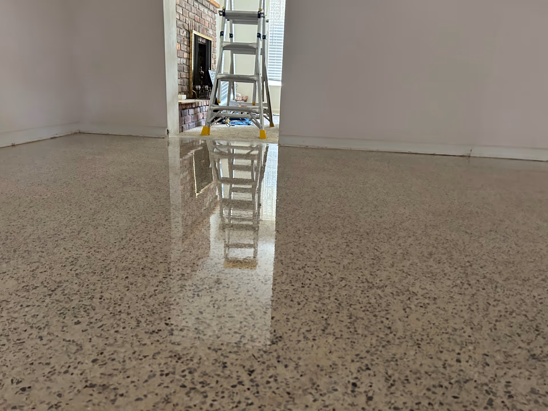 Interior room with a reflective polished floor, ladder near a brick fireplace.