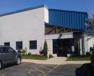Exterior view of a light-colored building with a blue awning and glass entrance.