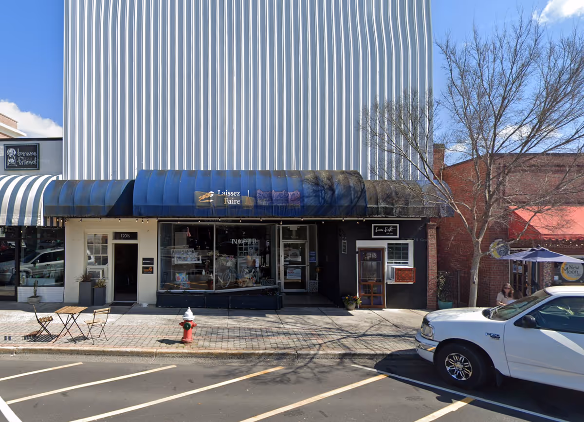 Street view of a storefront with blue awning, metal siding, outdoor seating, and a parked car.