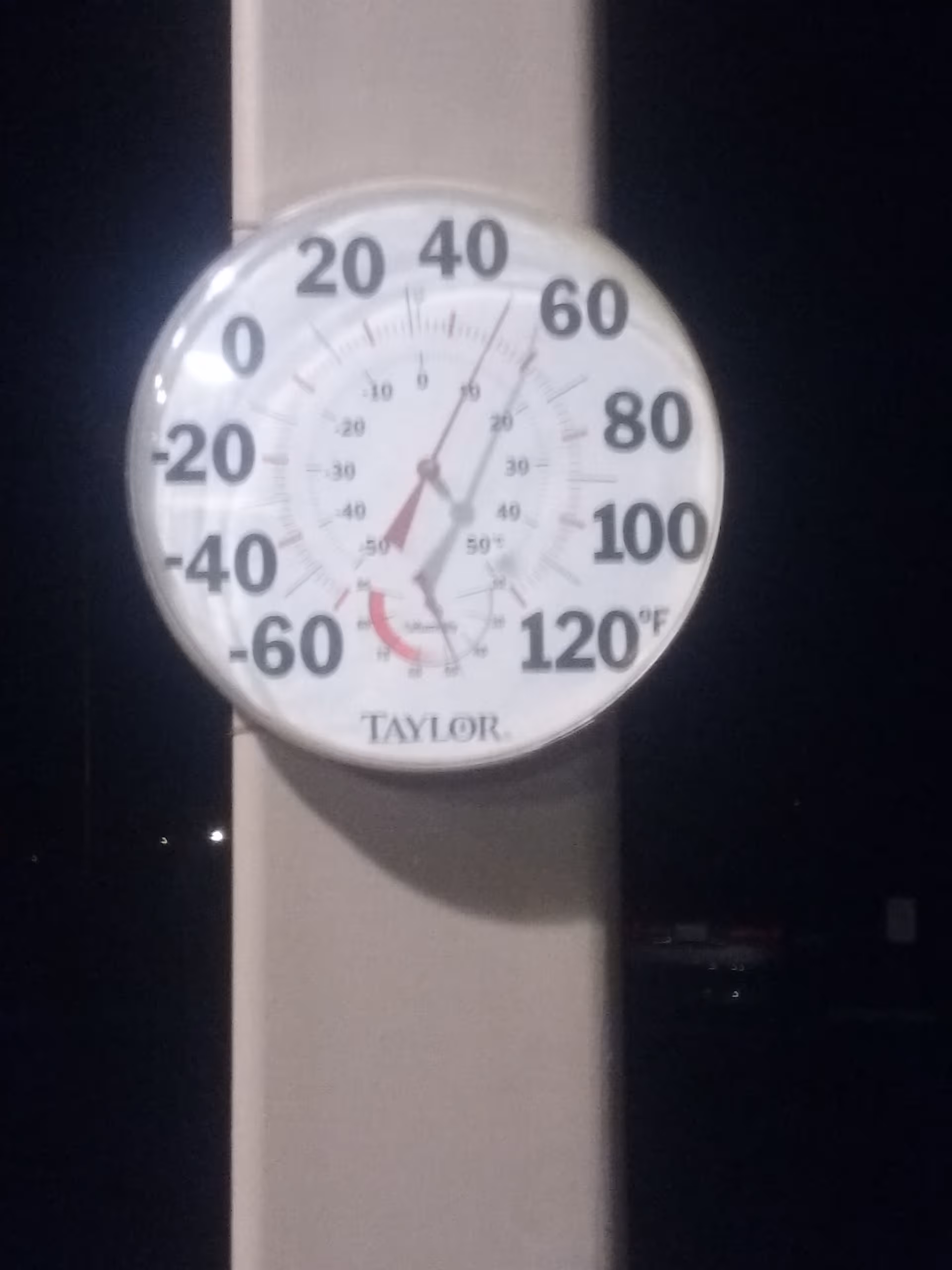 Round outdoor thermometer mounted on a post at night.