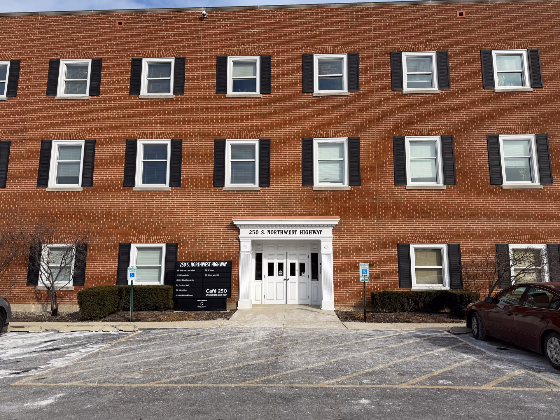 Brick multi-story senior living facility facade with white entry and parked cars.