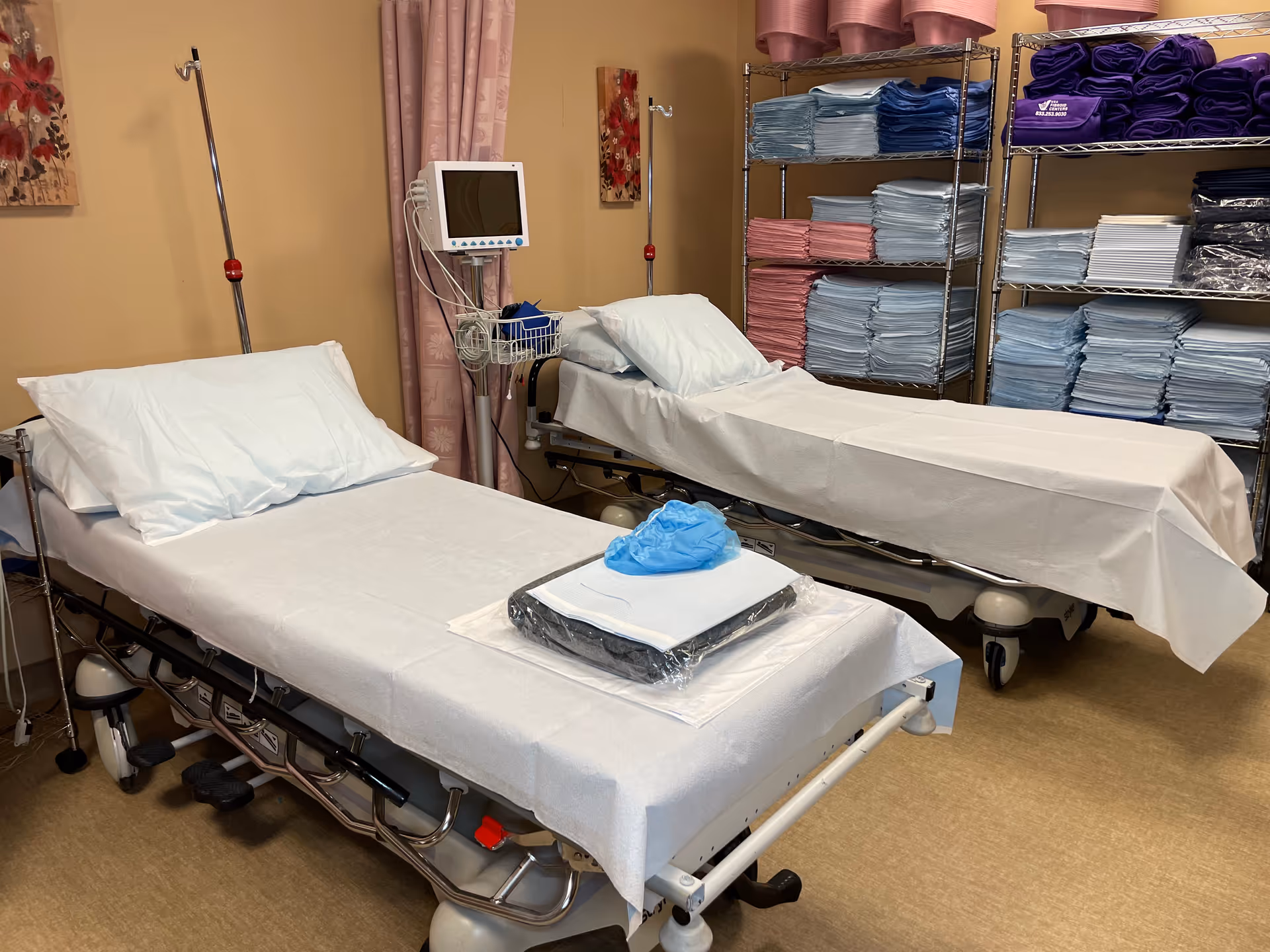 Two examination beds with linens and medical equipment in a clinical room.