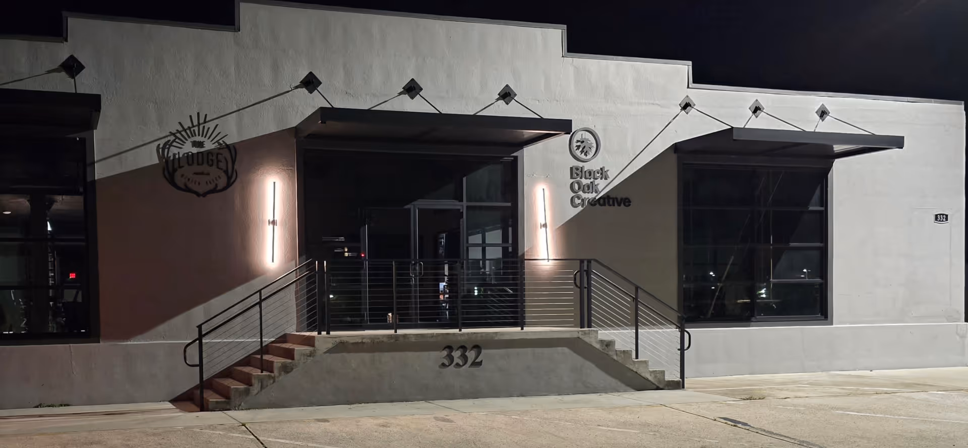 Nighttime view of a modern building front with stairs, railings, and large glass windows.