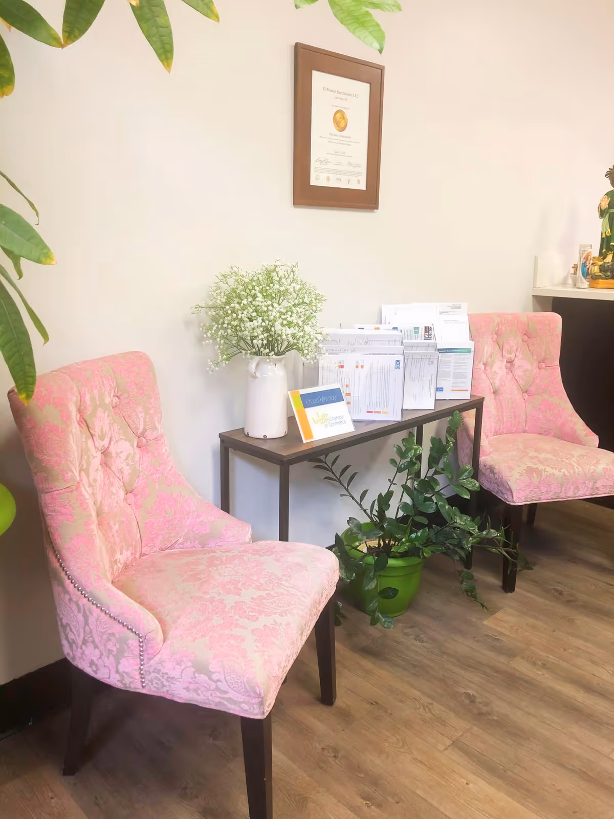 Two pink upholstered chairs flank a small table with brochures in a lobby.