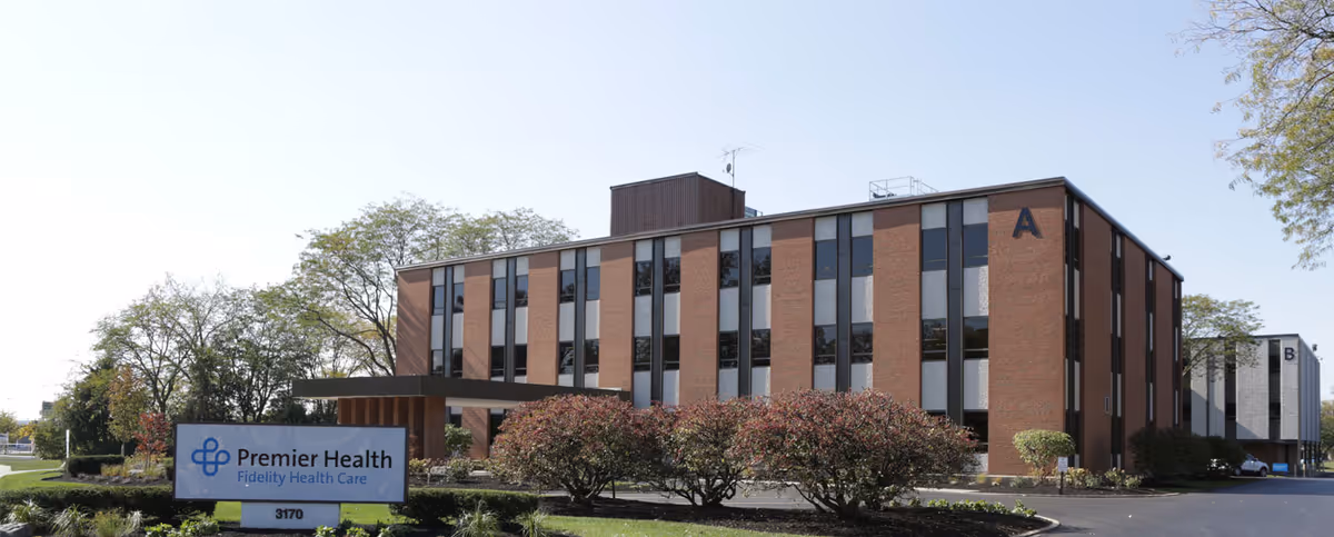 Brick senior living building exterior with a Fidelity Health Care sign and landscaped entry.