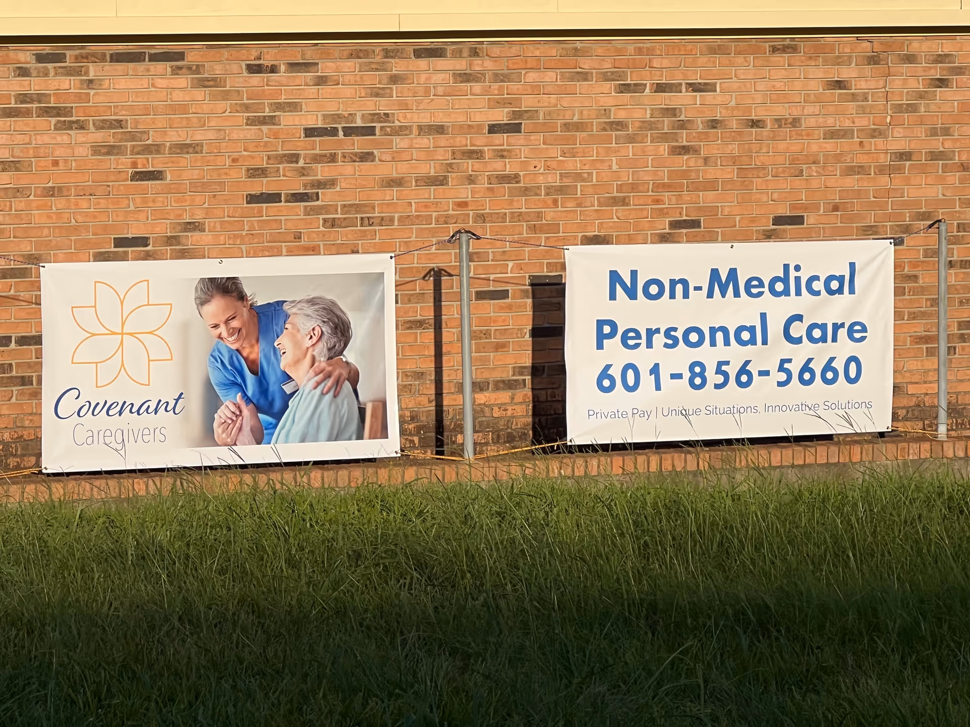 Two banners advertising Covenant Caregivers and non-medical personal care mounted on a brick exterior wall.