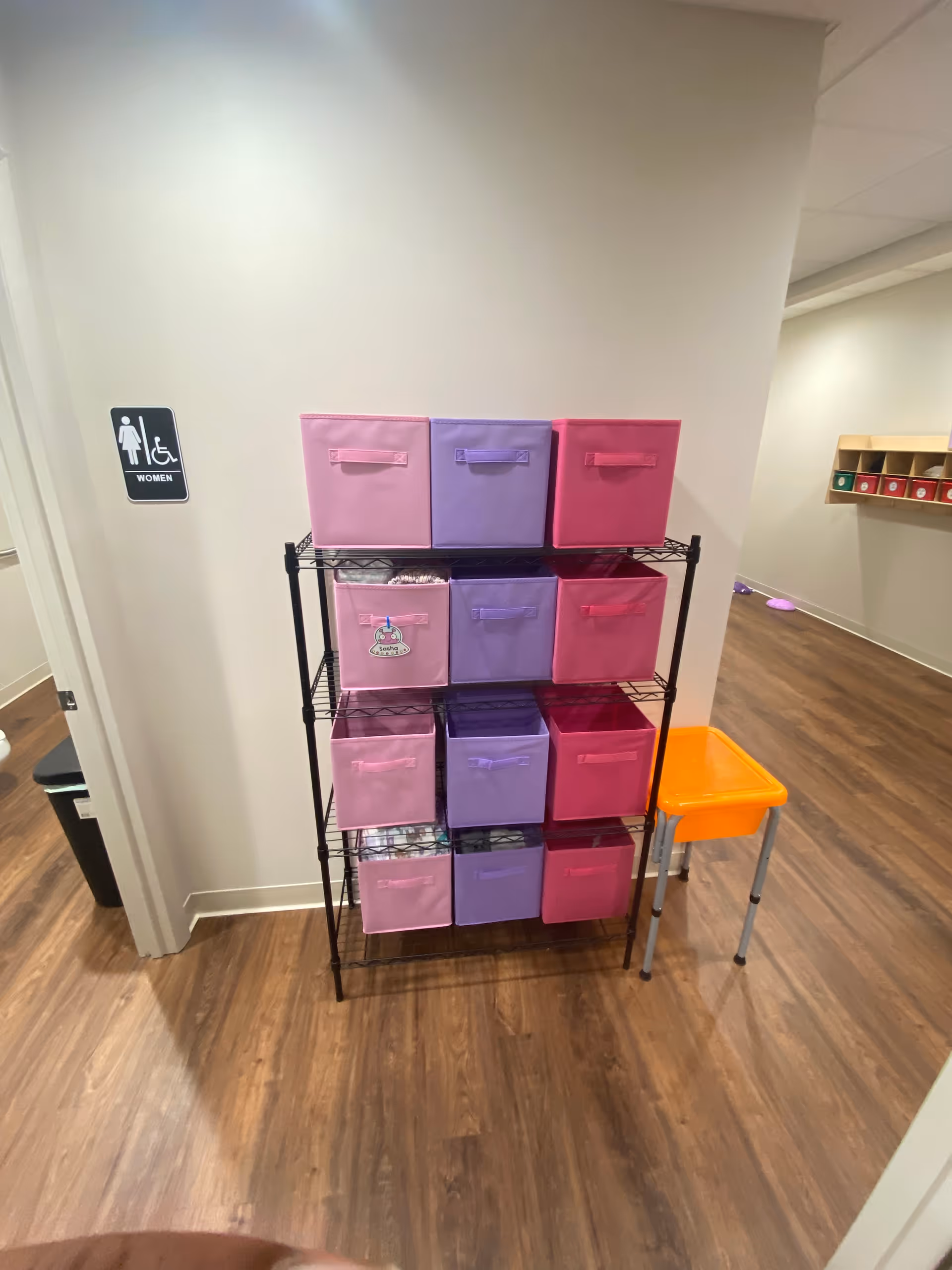 Indoor storage rack with pink and purple fabric bins in hallway corner.