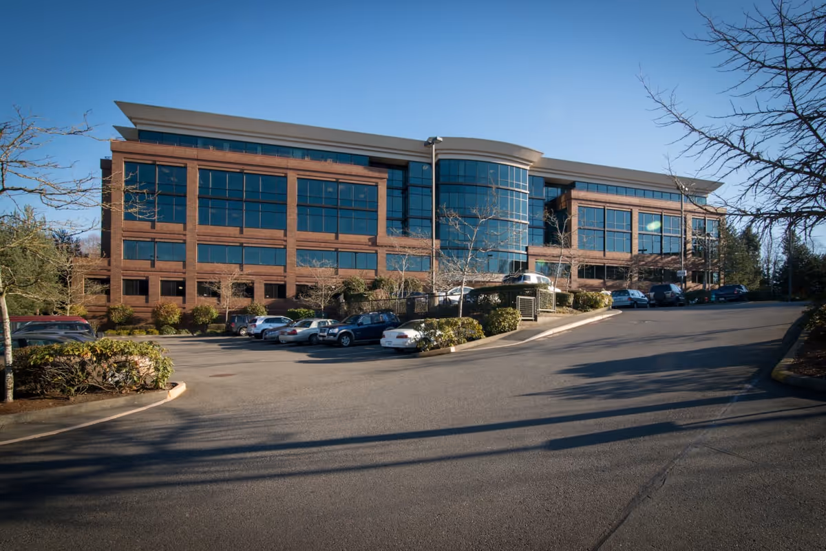 Brick building exterior with glass windows and a front parking lot.