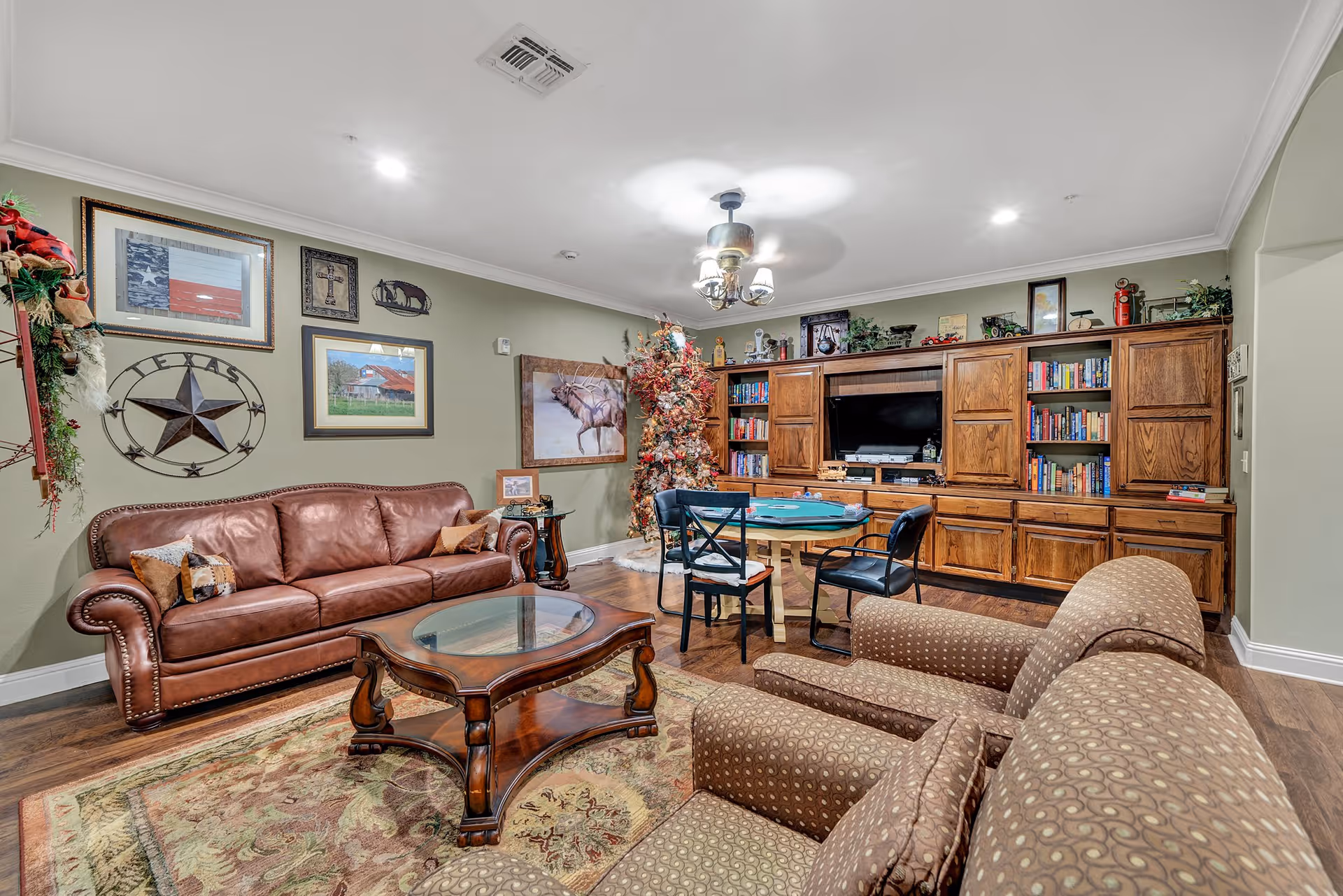 Spacious living room with a leather sofa and armchairs facing a large wooden entertainment wall, coffee table, and a card table.