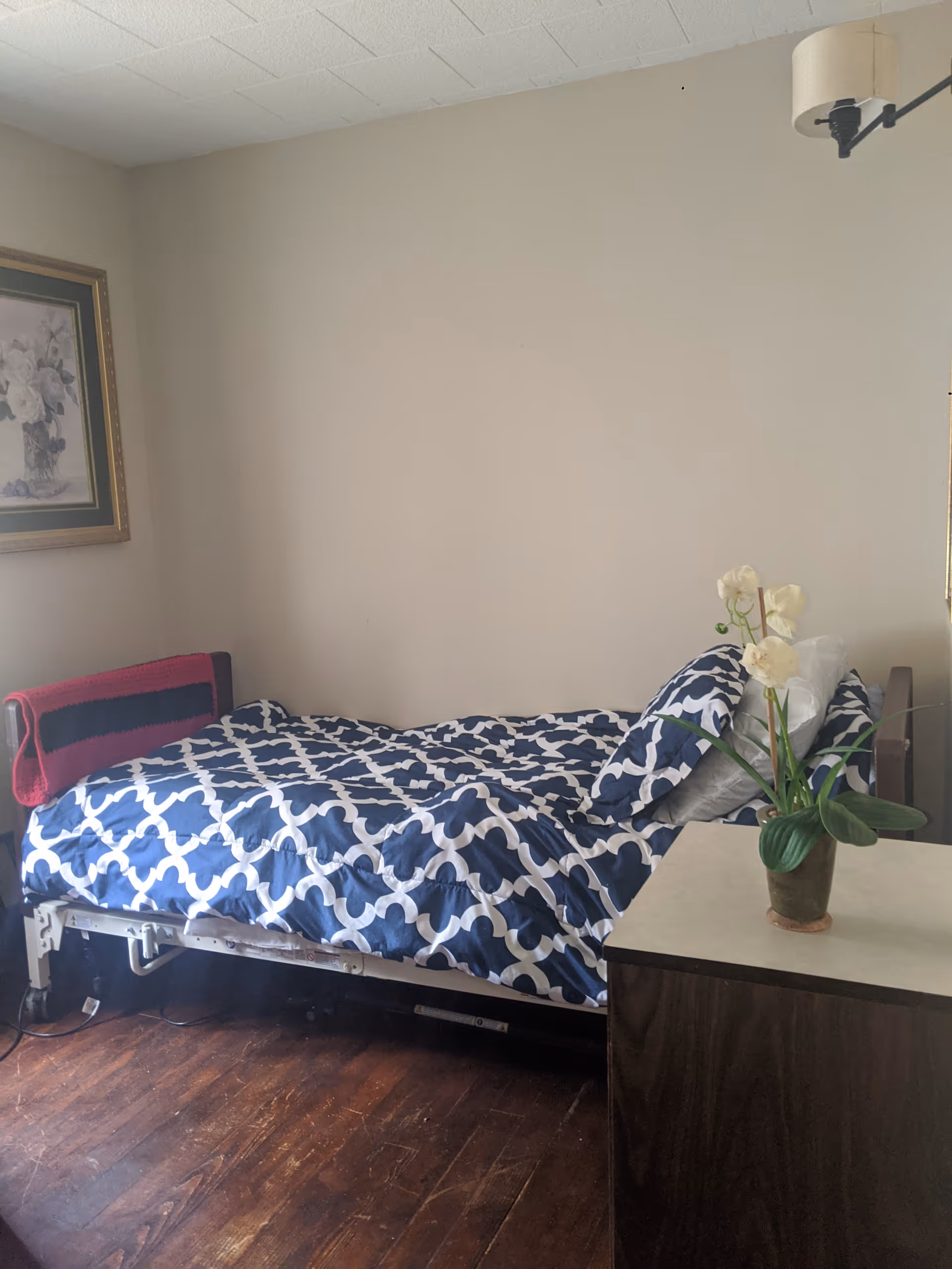 A small bedroom with a blue and white geometric comforter on a single bed and nightstand.