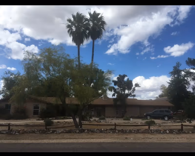 A single-story facility exterior with desert landscaping, palm trees, and a parked SUV.