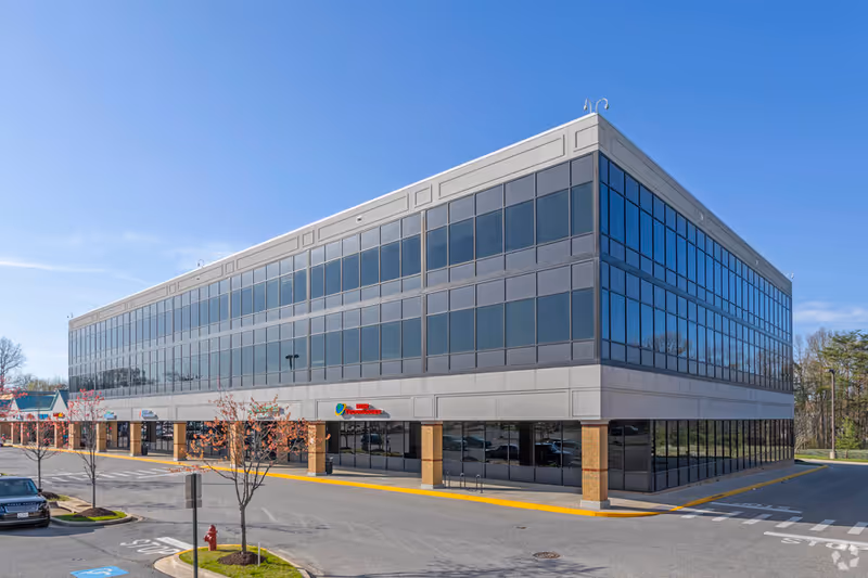 Modern glass-front senior living facility building with parking lot.