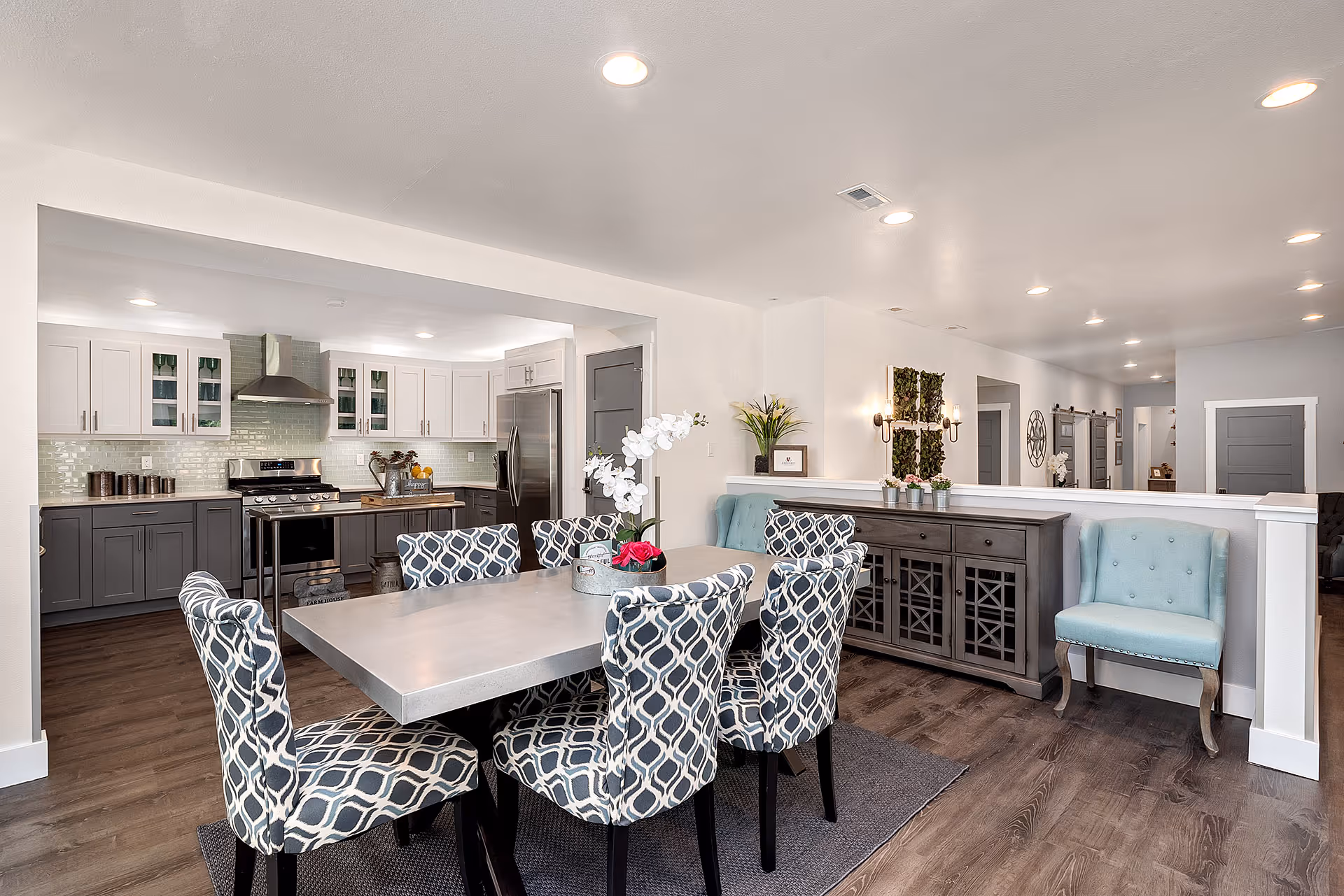 Open-concept dining area with patterned chairs, a gray sideboard, and a modern kitchen.