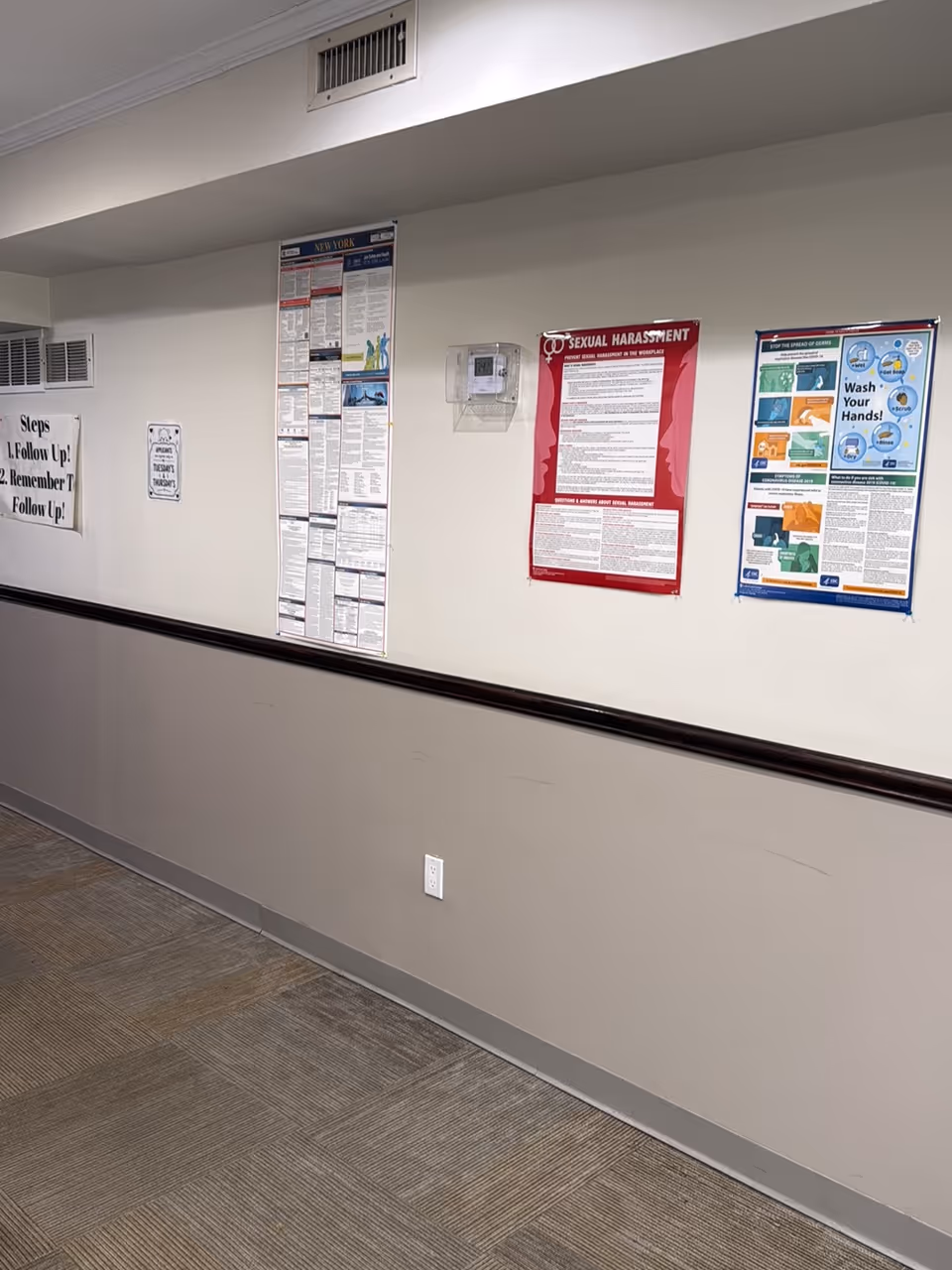 Interior hallway with multiple posters and a long handrail along the wall.