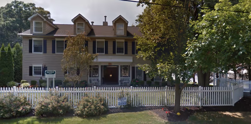 Two-story beige senior care building with white picket fence and front porch.