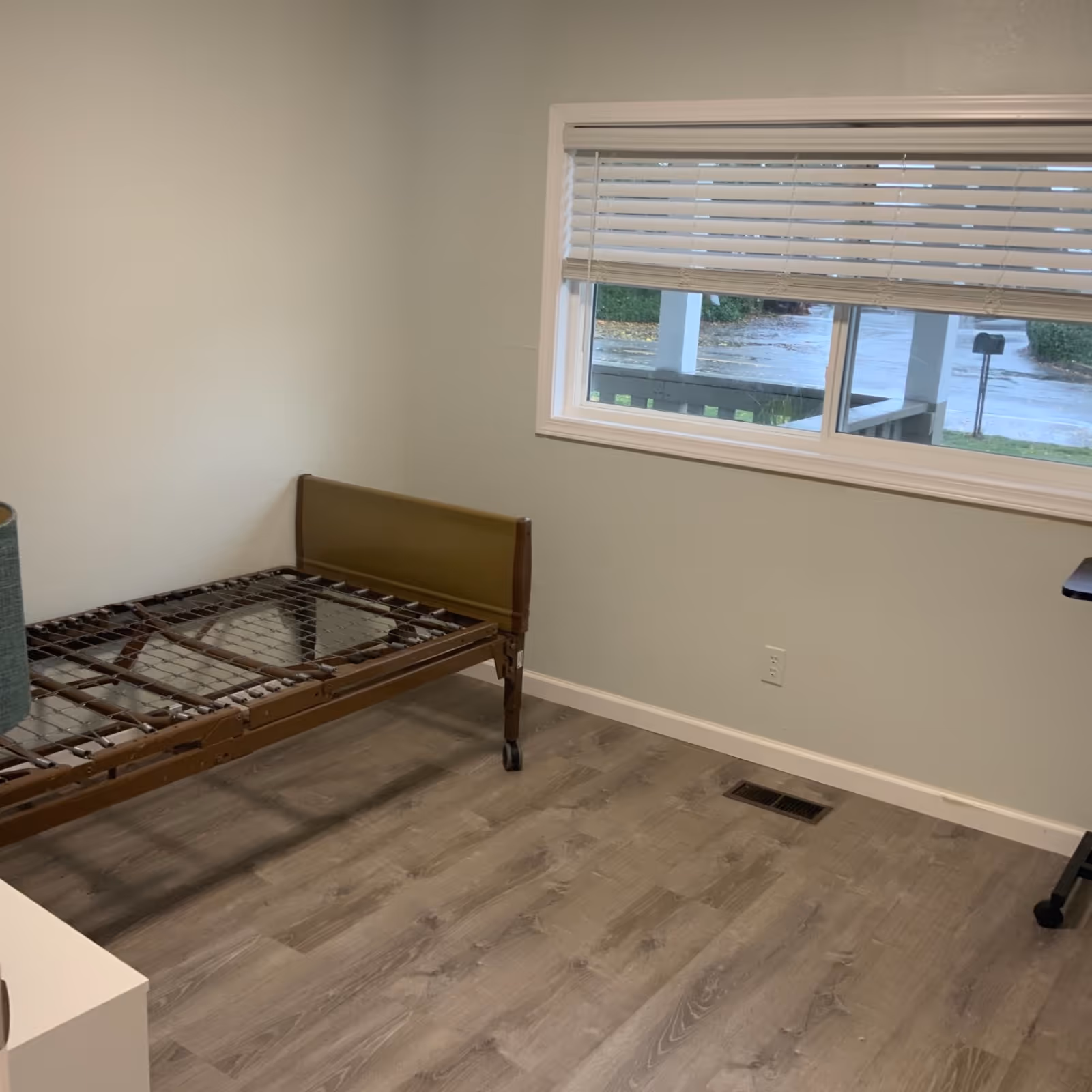 Empty bedroom in a senior facility with a metal bed frame and blinds.
