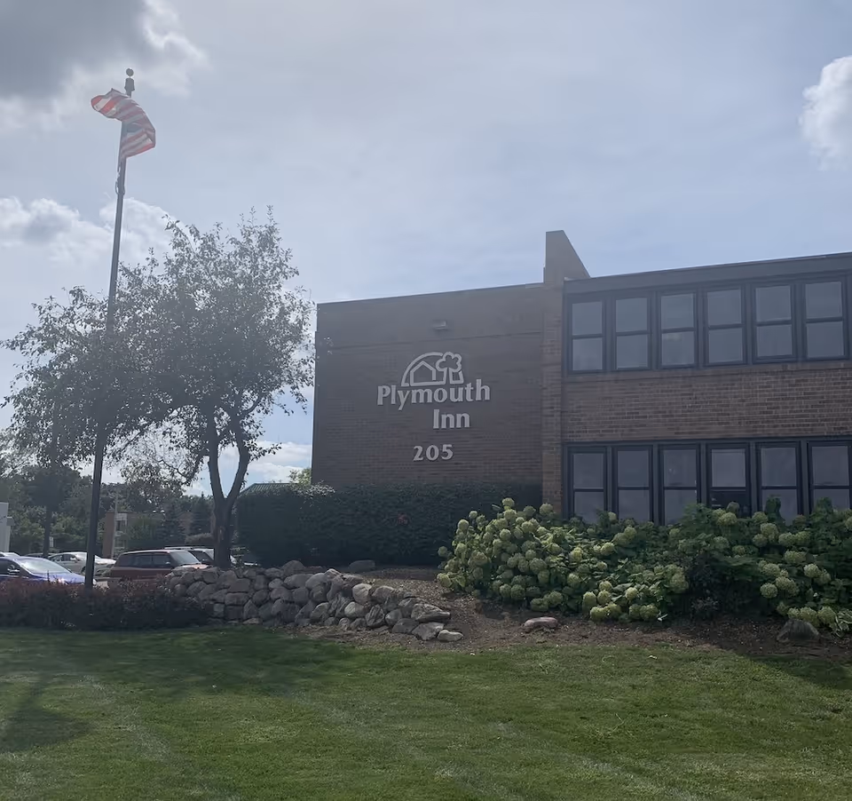 Front view of a brick building with a Plymouth Inn sign and landscaping.