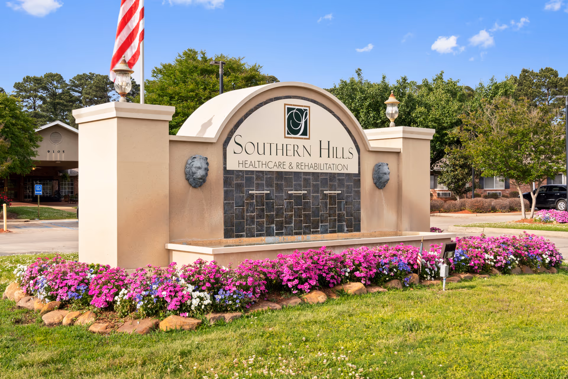 Entrance sign reading 'Southern Hills Healthcare & Rehabilitation' surrounded by flowers with an American flag and the facility buildings visible behind it.