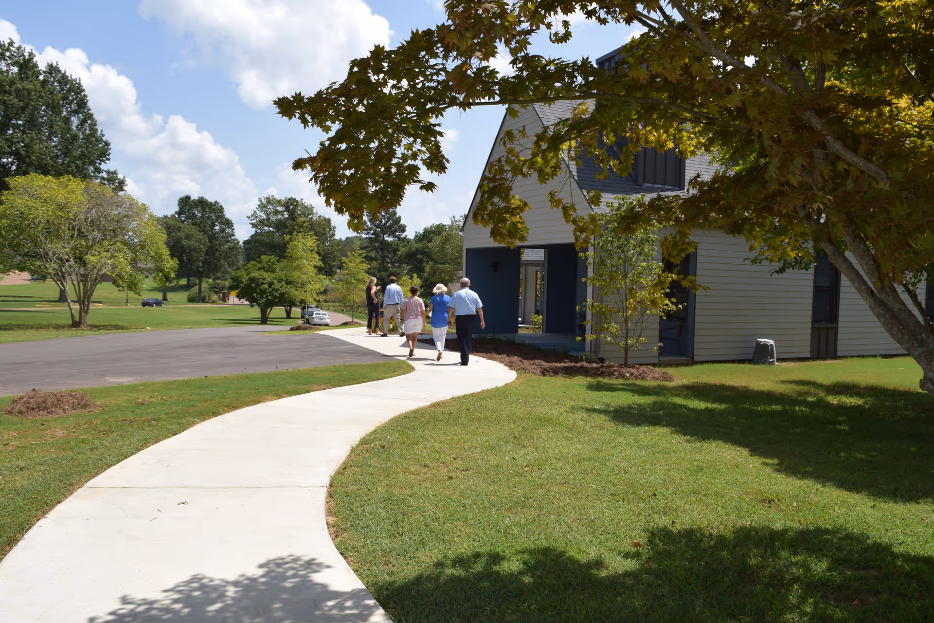 Group of people walking along a curved sidewalk toward the facility entrance amid trees.