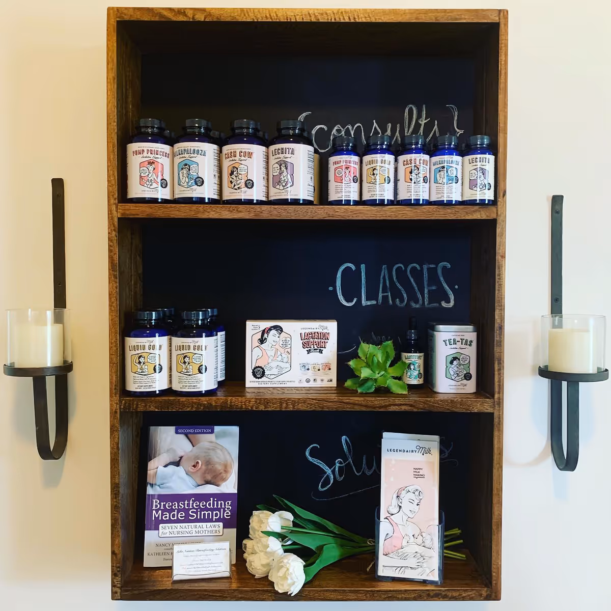 Two candle sconces flank a wooden display shelf filled with lactation products