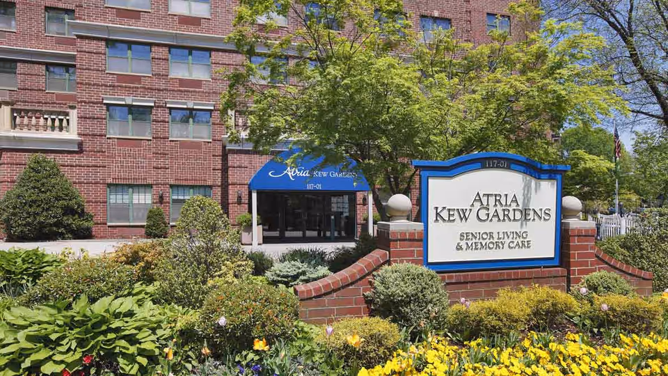 Exterior view of Atria Kew Gardens senior living with sign and landscaping.