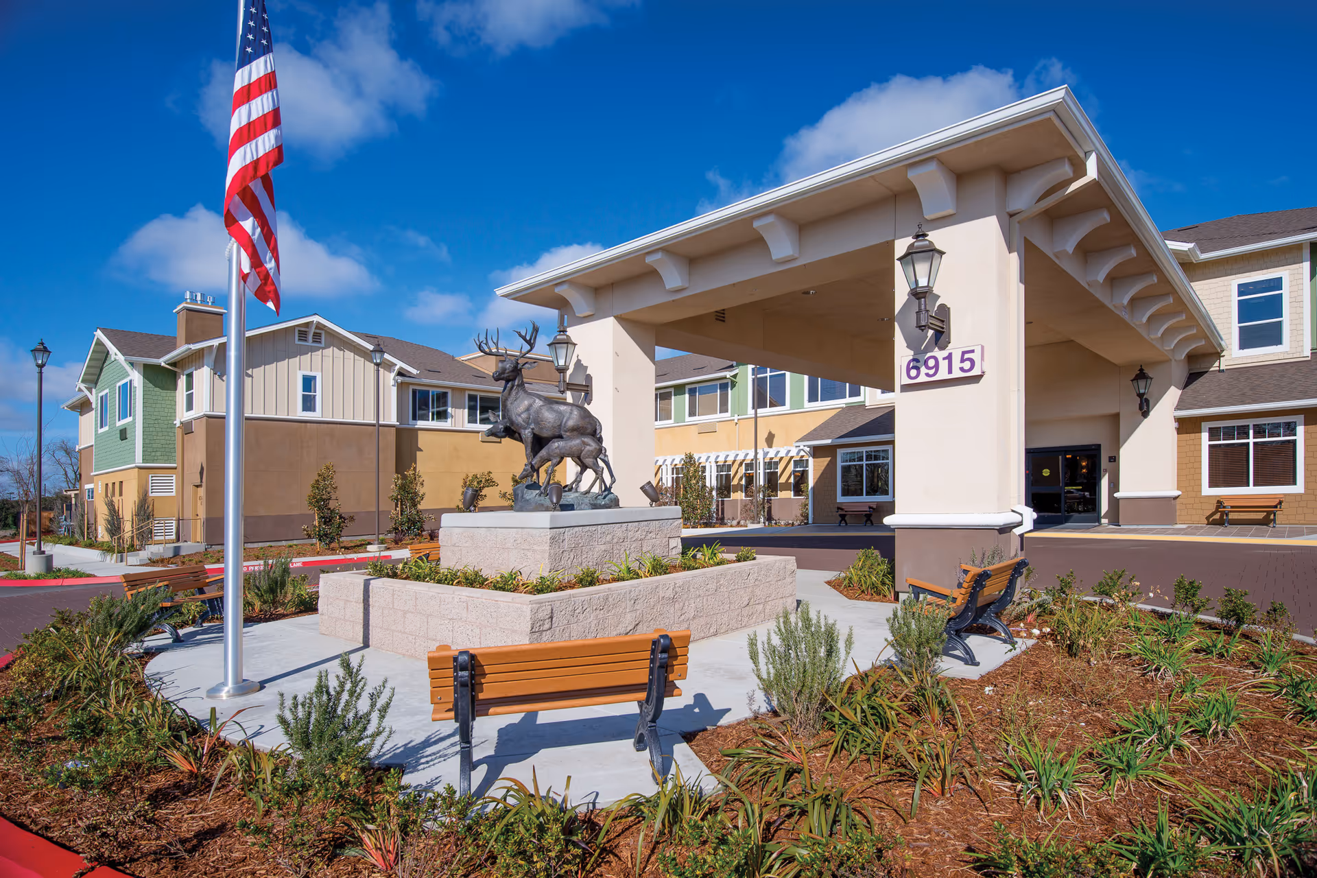 Exterior view of Carlton Senior Living Elk Grove with flag, statue, and entrance.