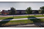 Long, low brick building along a tree-lined street with a sidewalk.