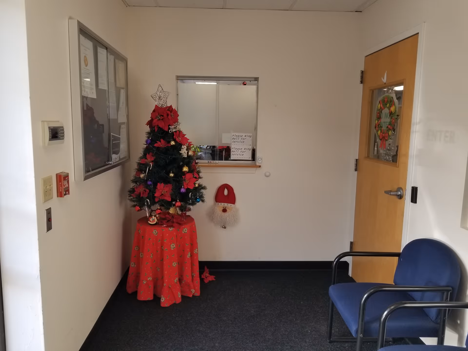 Small interior hallway with a Christmas tree, service window, wreath, and blue chairs.