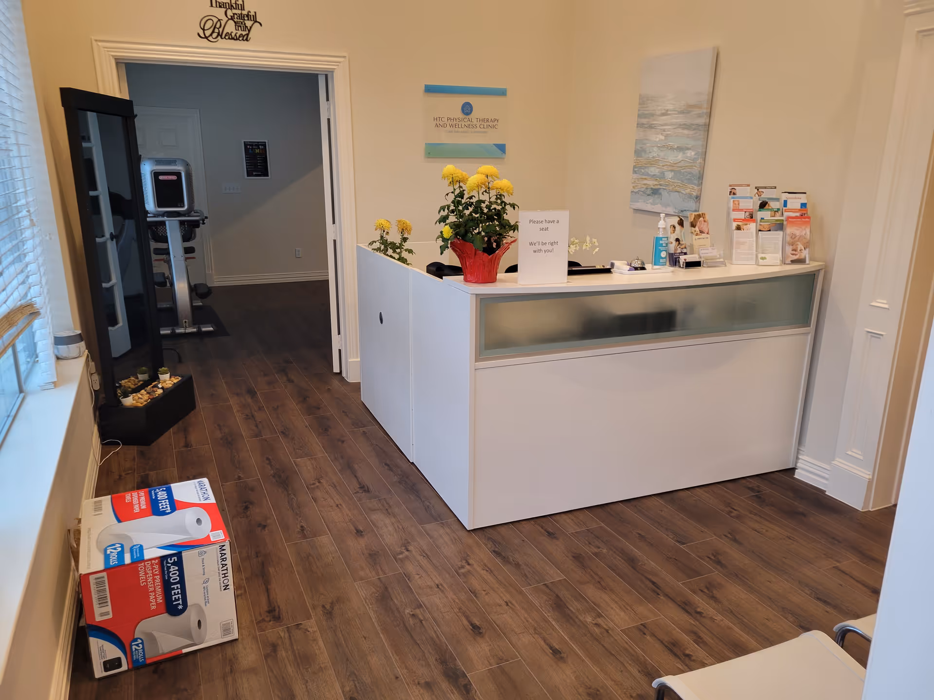 Lobby reception desk inside a senior living facility, with brochures, plants, and exercise equipment visible.