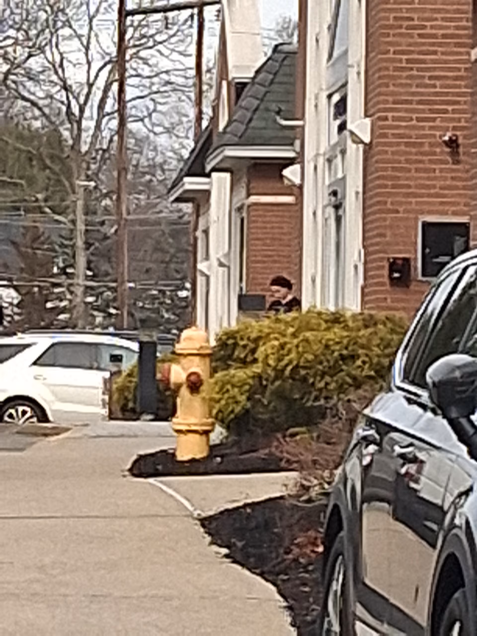 Brick senior living building exterior with parked cars and a yellow fire hydrant along the sidewalk.