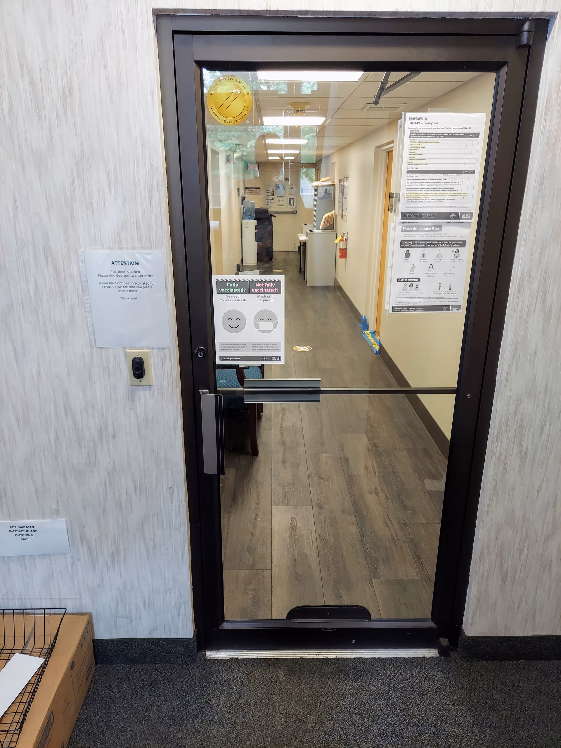 Glass door opens to a clinical hallway with equipment, posters, and a reception area visible.