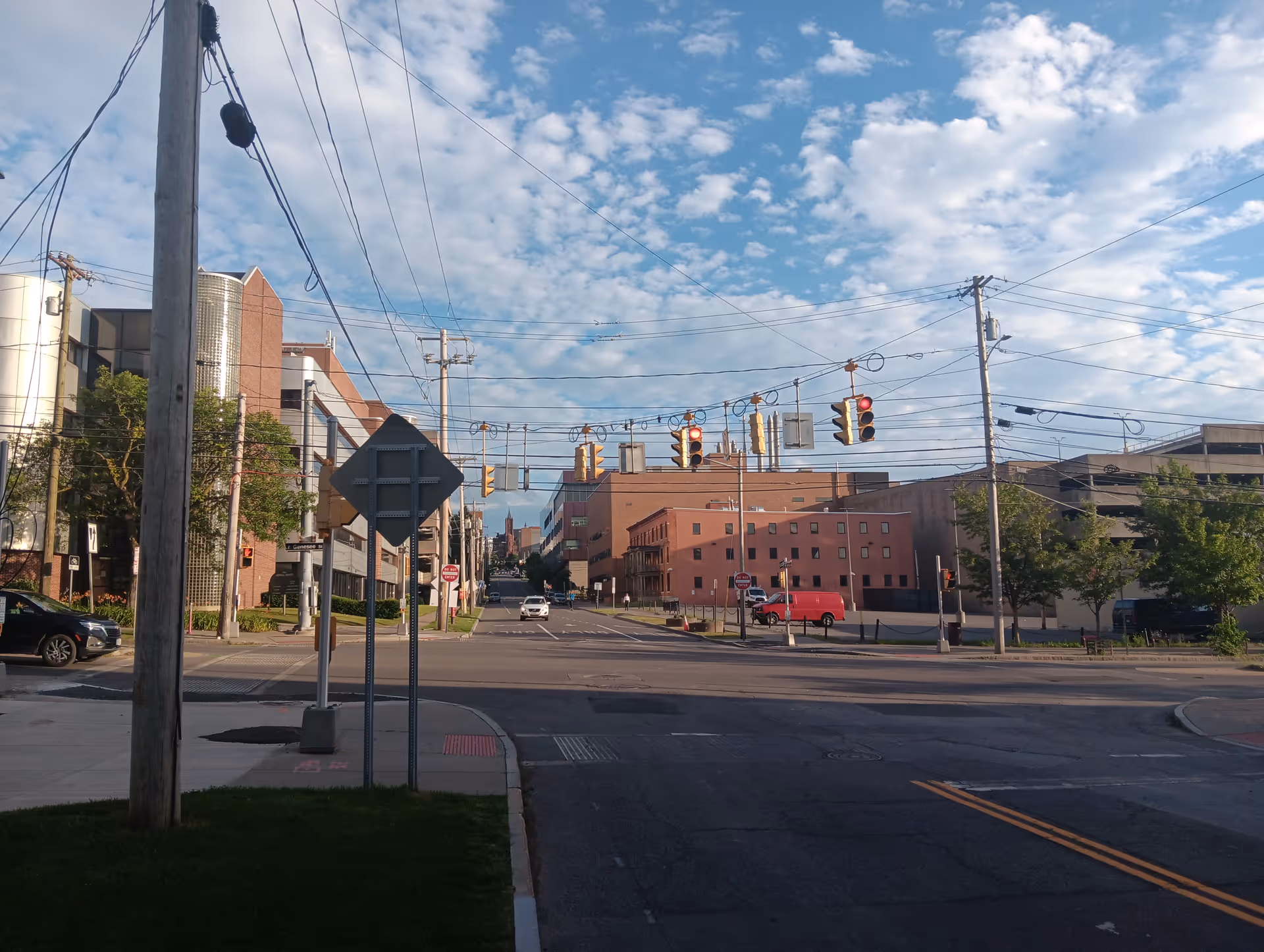 City street intersection with traffic signals, power lines, and brick buildings under blue sky